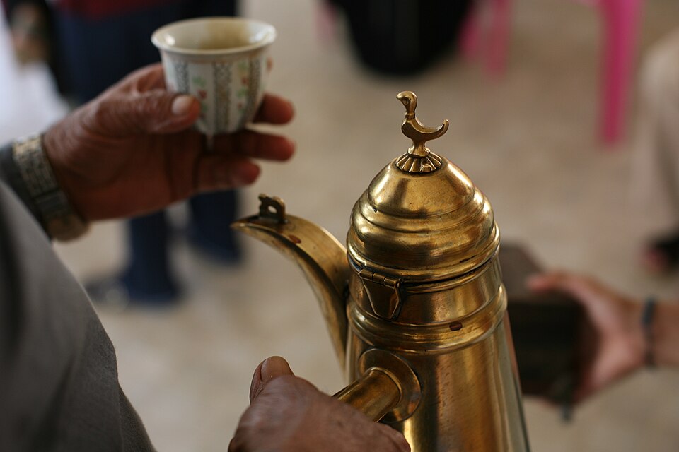 Arabic coffee being poured from a brass dallah into a small cup